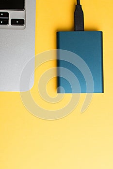 Vertical shot of an external memory drive and a laptop edge on yellow background