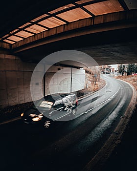 Vertical shot of a fast car in motion on a road under a bridge