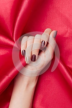 Vertical shot of a female\'s hand with beautiful nail polish caressing a red silk fabric