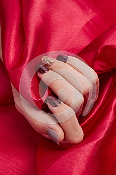 Vertical shot of a female's hand with beautiful nail polish caressing a red silk fabric