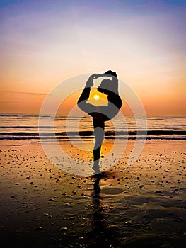 Vertical shot of a female silhouette doing the Natarajasana yoga pose at the beach with the sunset