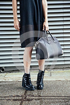 Vertical shot of a female wearing a black dress and holding a black bag under the sunlight