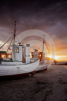 Vertical shot of fishing boats under the cloudy skies during the sunset