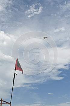 Vertical shot of the flag of dangerous waters on a beach with a plane flying over it