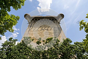 Vertical shot of a Flak tower surrounded by trees under the cloudy blue sky in Vienna, Austria