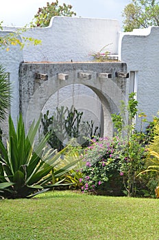 Vertical shot of flowers and plants near a small stone arch beside a white wall