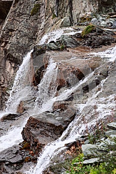 Vertical shot of flowing and foaming water of alpine waterfall against background of granite rocks of various textures and colors