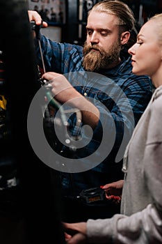 Vertical shot of focused bearded cycling repairman communicating with female client, showing problem of bicycle