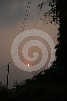 Vertical shot of a full moon in a cloudy sky with silhouettes of trees and power electric lines