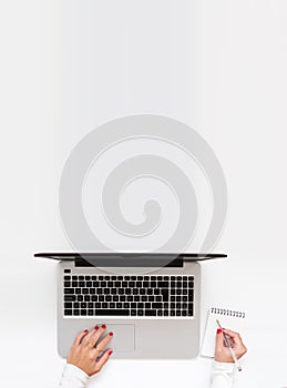 Vertical shot of girl hands typing and writing notes. Top view, flat lay, girl working at home while telecommuting with copy space