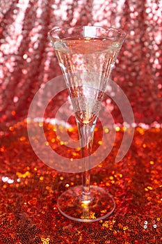 Vertical shot of a glass of champagne with red glitter background