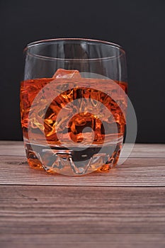 Vertical shot of a glass of whiskey with ice on a wooden table - perfect for drink concepts