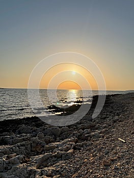 Vertical shot of the golden sunset shining over the calm sea and the rocky shore