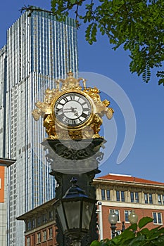 Vertical shot of a golden watch behind a skyscraper