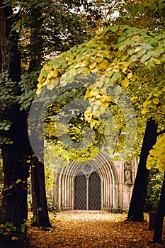 Vertical shot of a gothic grave surrounded by fall trees in a cemetery in Berlin, Germany