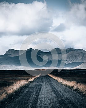 Vertical shot of a gravelroad leading towards the scenic mountains in the majestic Iceland