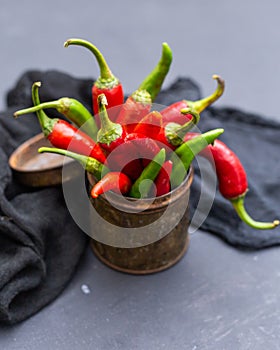 Vertical shot of the green and red hot chili peppers in a rusty cup with cloth on a dark tabletop