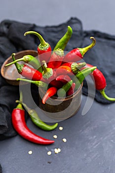 Vertical shot of the green and red hot chili peppers in a rusty cup with cloth on a dark tabletop