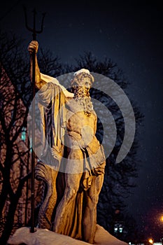 Vertical shot of a half-naked male sculpture with a long beard holding a wand during nighttime