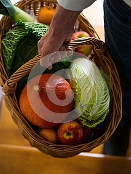 Vertical shot of a hand carrying a wicker basket full of healthy fruits and vegetables