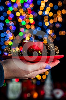 Vertical shot of a hand holding a Christmas candle decoration against bokeh lights background
