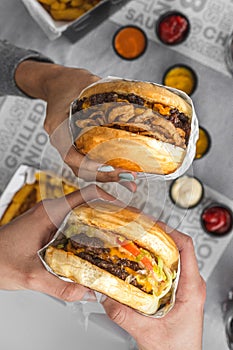 Vertical shot of hands holding delicious juicy burgers over a table with sauces