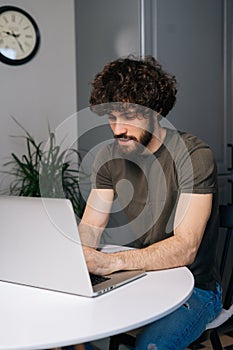 Vertical shot of handsome bearded young business man using typing laptop keyboard, writing email or message sitting at