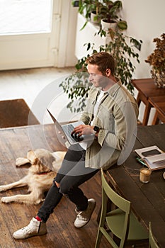 Vertical shot of handsome businessman, young man with laptop leans on table, sitting at co-working space with his dog