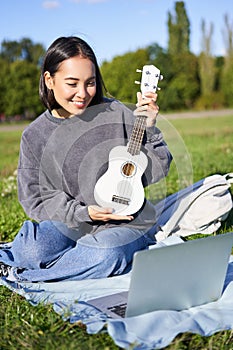 Vertikální z šťastný asijský hraje nástroj ukazuje její hudební nástroj na přenosný počítač chatování o hudba učí 
