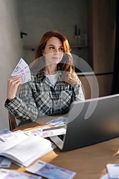 Vertical shot of happy businesswoman holding banknotes of dollars in and fanning money in front of face. Successful