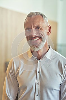 Vertical shot of a happy mature businessman in classic wear looking at camera and smiling while standing in the office