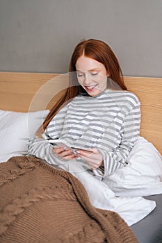 Vertical shot of happy young woman enjoy shopping online with credit card and mobile phone lying in bed at home.