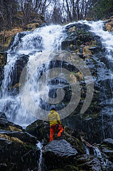 Vertical shot of a hiker standing under the waterfall on the rocks in a forest