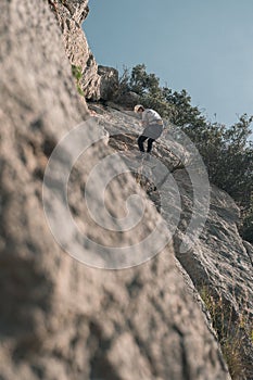 Vertical shot of a Hispanic male with a white shirt and helmet climbing the mountains