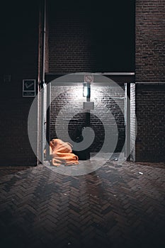 Vertical shot of a homeless person sleeping under an orange blanket in front of a building