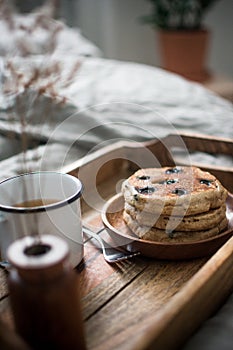Vertical shot of homemade pancakes with a cup of tea on a wooden tray near the bed. Breakfast in bed