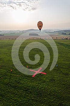 Vertical shot of a hot air balloon landing in a green grass field with landing spot marked by X