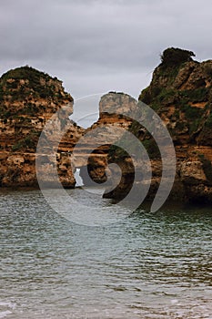 Vertical shot of huge rock formations in the sea by Praia do Camilo beach