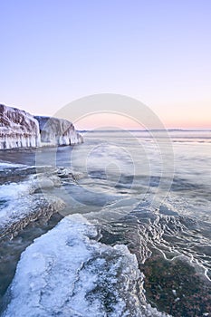 Vertical shot of an idyllic frozen rocky shore with pink sky on the horizon, perfect for wallpapers