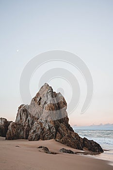 Vertical shot of an idyllic sandy coast with rocky cliffs at sunset