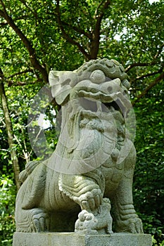 Vertical shot of Japanese stone lion statue in the park with green trees in the background