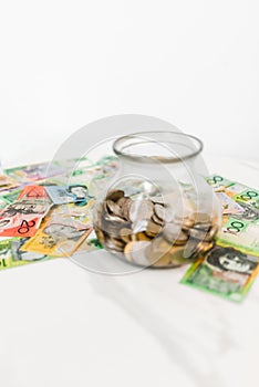 Vertical shot of a jar with coins and Australian dollar banknotes on the white background