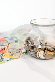 Vertical shot of a jar with coins and Australian dollar banknotes on the white background