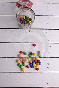 Vertical shot of a jar with colorful candies half-emptied on a wooden table