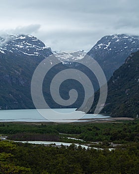 Vertical shot of a lake surrounded with high forested mountains on a cold winter day