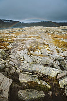 Vertical shot of land with a lot of rock formations and the rainbow in background in Finse, Norway