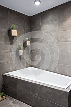 Vertical shot of a large comfortable luxurious white bath in a cozy bathroom with stylish grey stone walls and wall flower pots