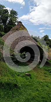 Vertical shot of the late iron age roundhouse in the grass surrounded by trees during the daytime