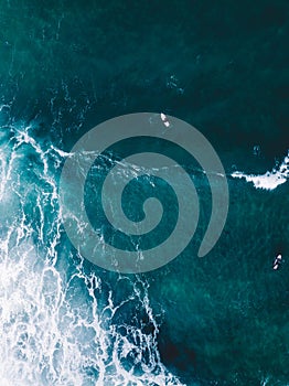 Vertical shot of lazur ocean waters with distanced boats and a corner of wavy white foam photo