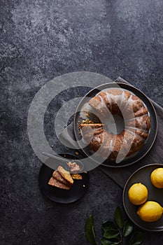 Vertical shot of lemon cake covered with sweet sauce near a plate of lemons on a black surface